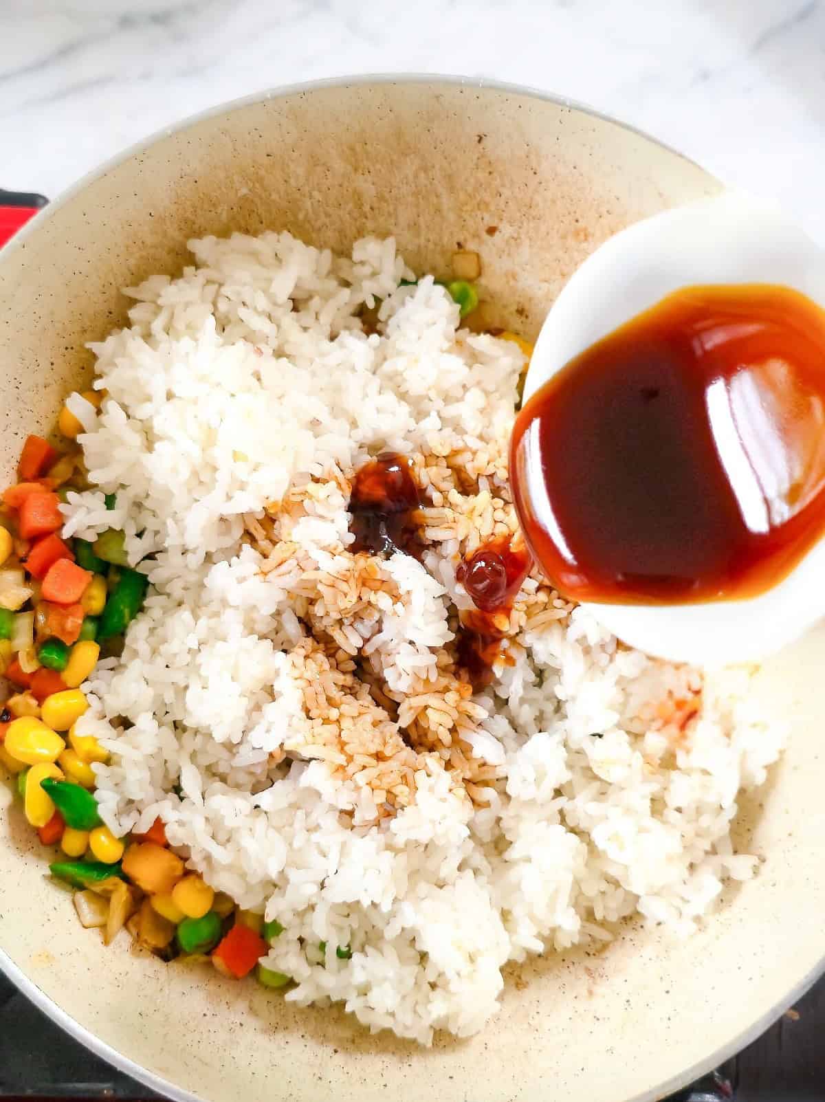 Cooked rice added to vegetables as sauce is poured into the pan.