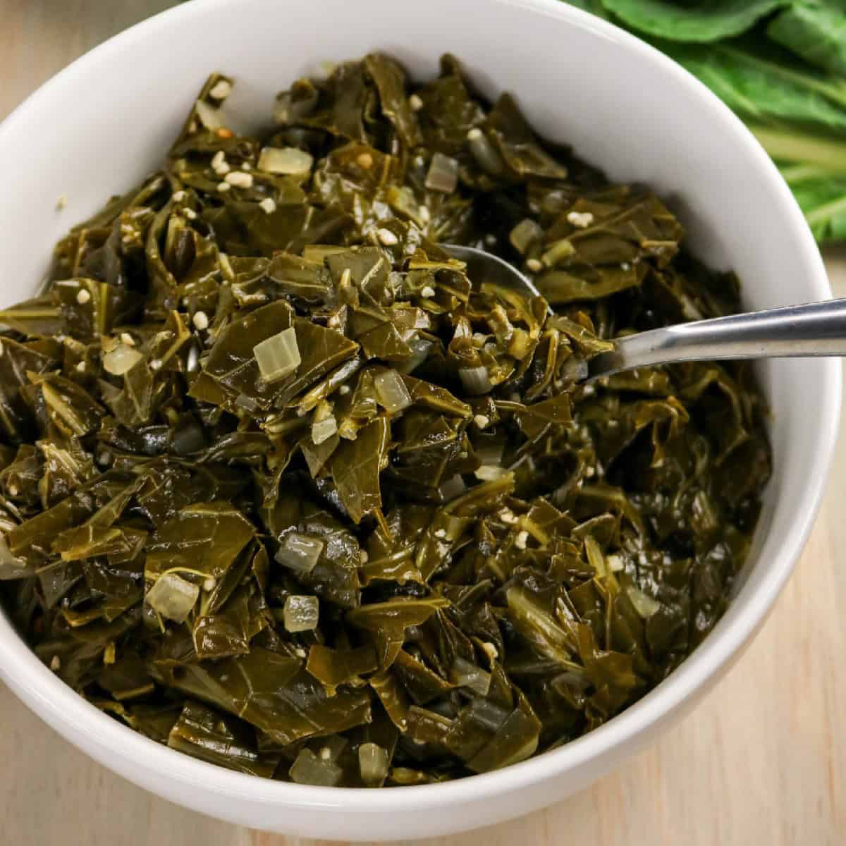 Braised collard greens served in a bowl with a spoon on a light surface.