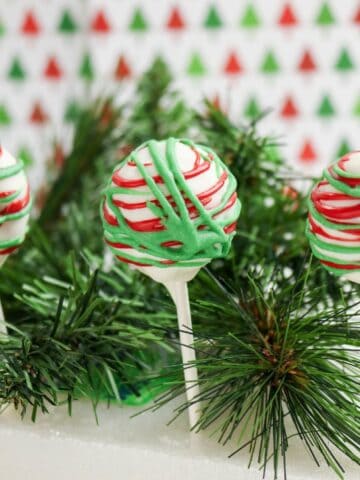 Christmas cake pops decorated with red and green drizzle on white chocolate coating.