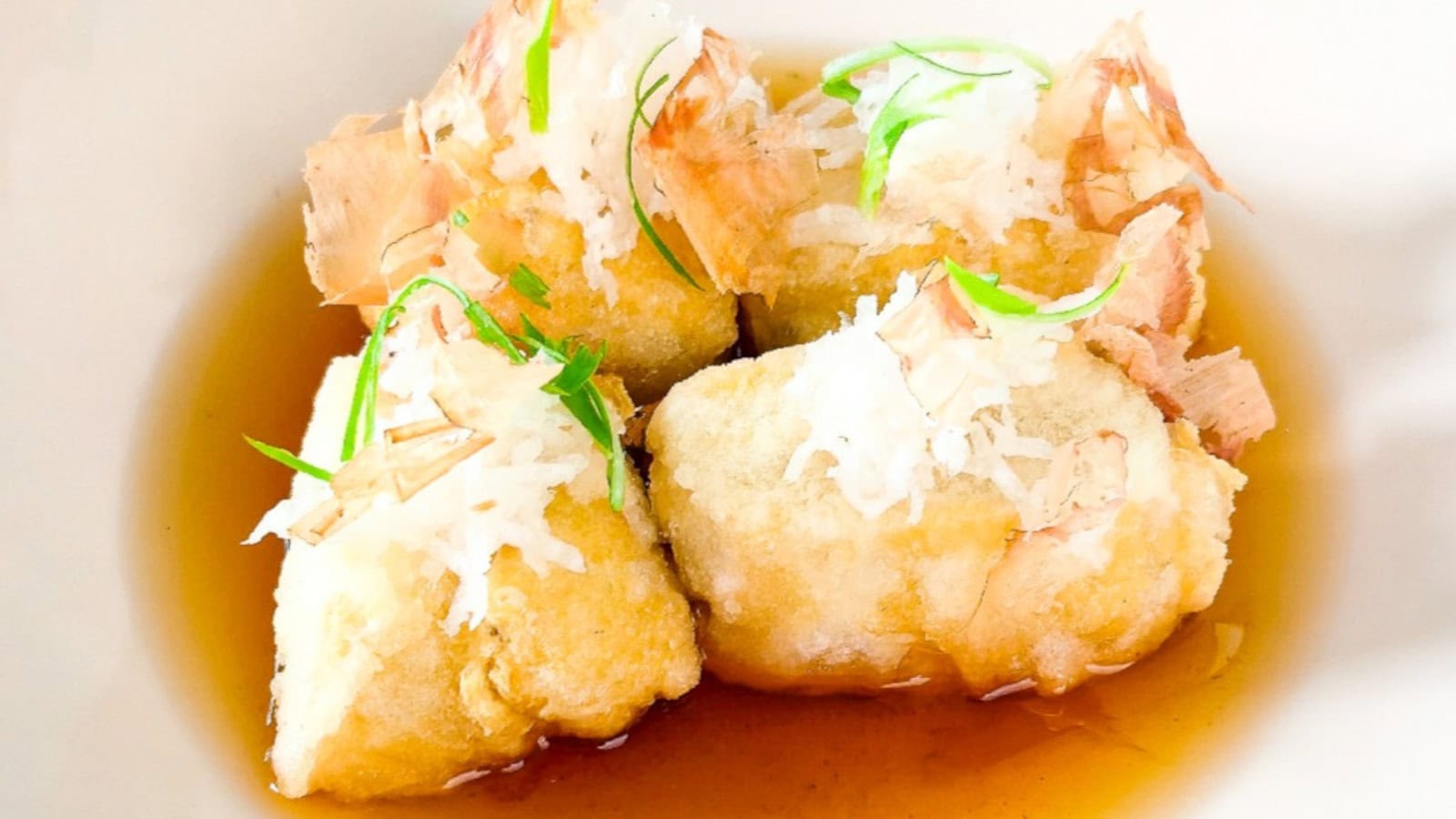 Japanese agedashi tofu in dashi broth, topped with grated daikon, green onions, and bonito flakes.