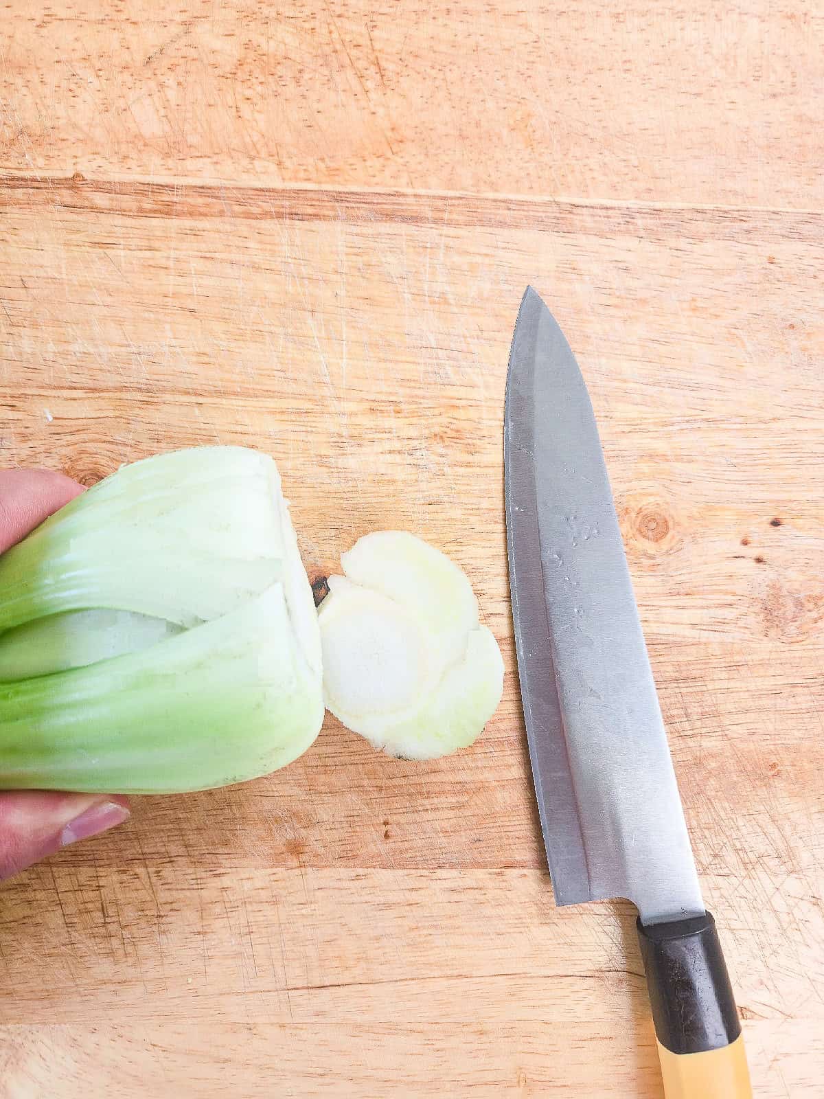 Cutting the base off fresh bok choy on a wooden cutting board.