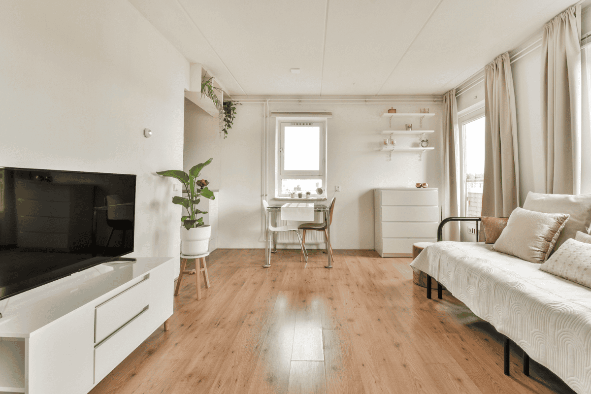 Minimalist living area with a sofa, TV console, small desk, light wood floors, and natural light.