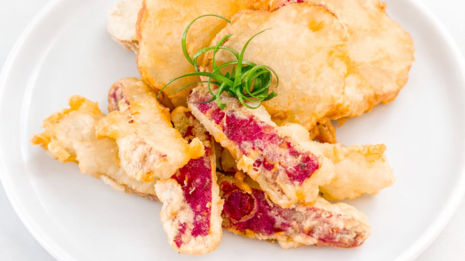 Crispy sweet potato tempura with red-skinned slices on a white plate.