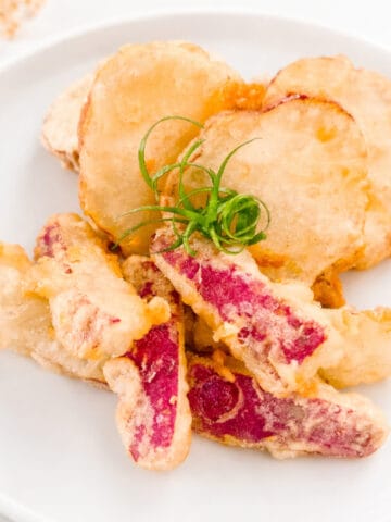 Crispy sweet potato tempura with purple-skinned slices on a white plate, garnished with green onions.