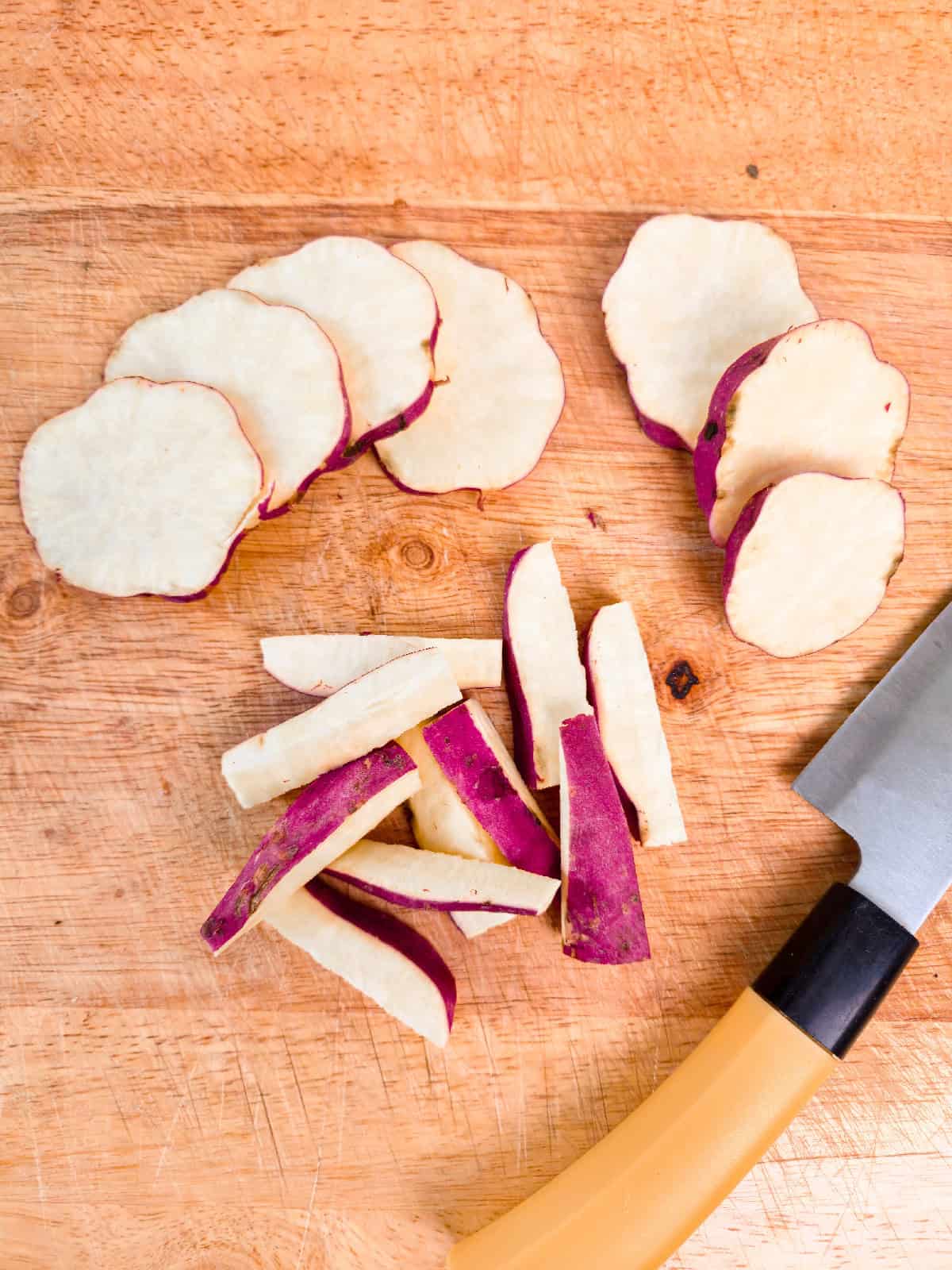 Sweet potatoes sliced into thin rounds and batons on a wooden cutting board.