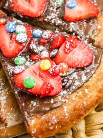 Chocolate Nutella pizza topped with fresh strawberry slices, colorful candy pieces, and powdered sugar on a cinnamon-sugar crust.