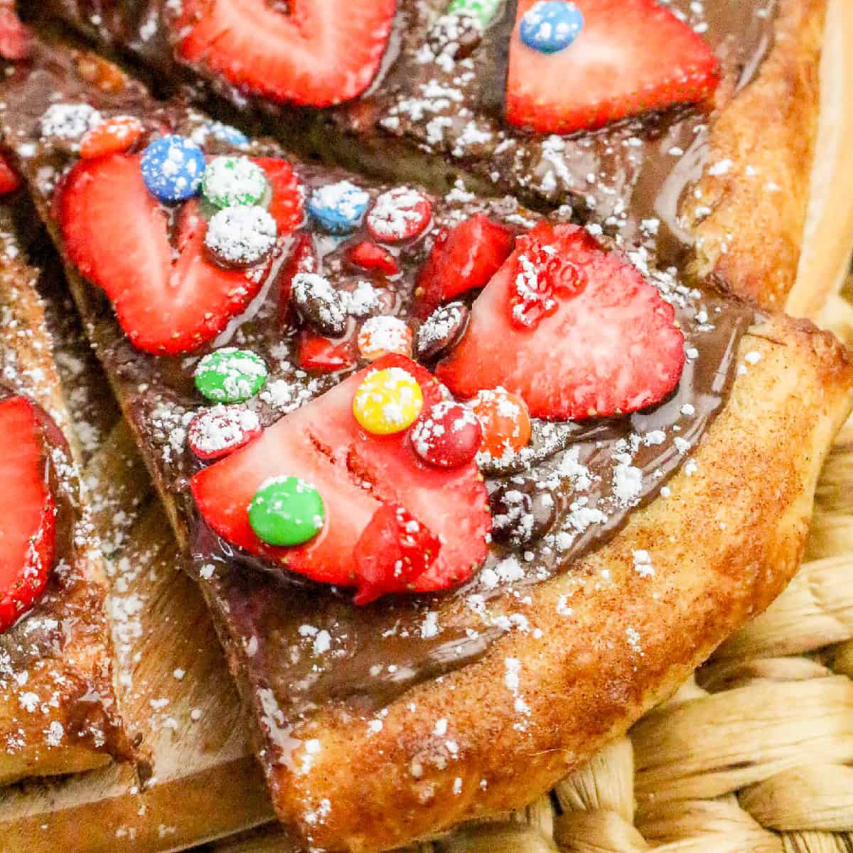 Chocolate Nutella pizza topped with fresh strawberry slices, colorful candy pieces, and powdered sugar on a cinnamon-sugar crust.
