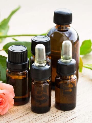 Brown glass essential oil bottles displayed with pink roses and green foliage on a wooden table.