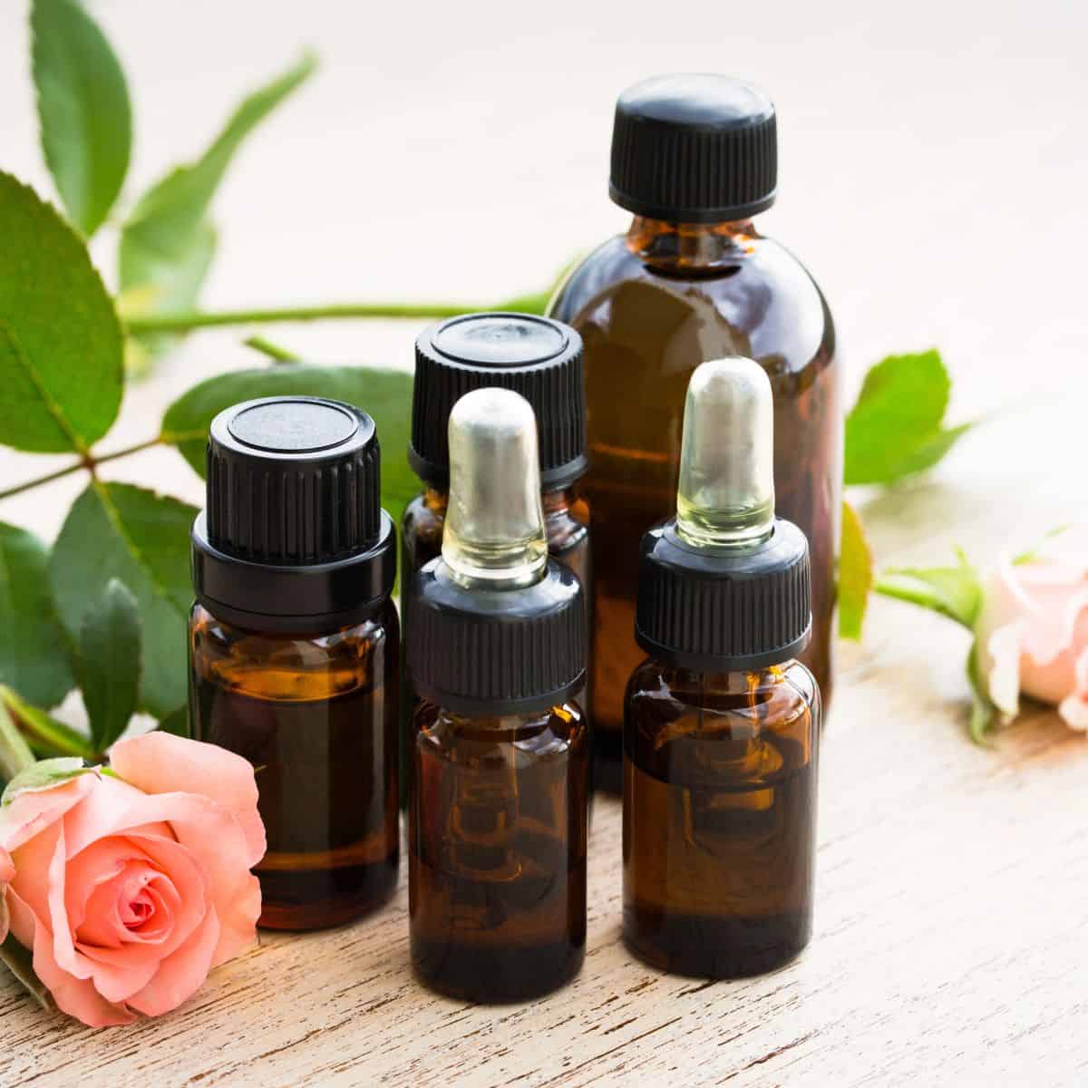 Brown glass essential oil bottles displayed with pink roses and green foliage on a wooden table.