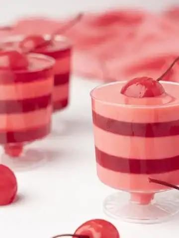 Cherries and cream layered jello shots for valentines day on a white table.