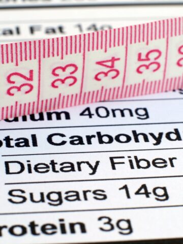 Measuring tape laid across a nutrition label highlighting total carbohydrates, fiber, sugars, and protein.