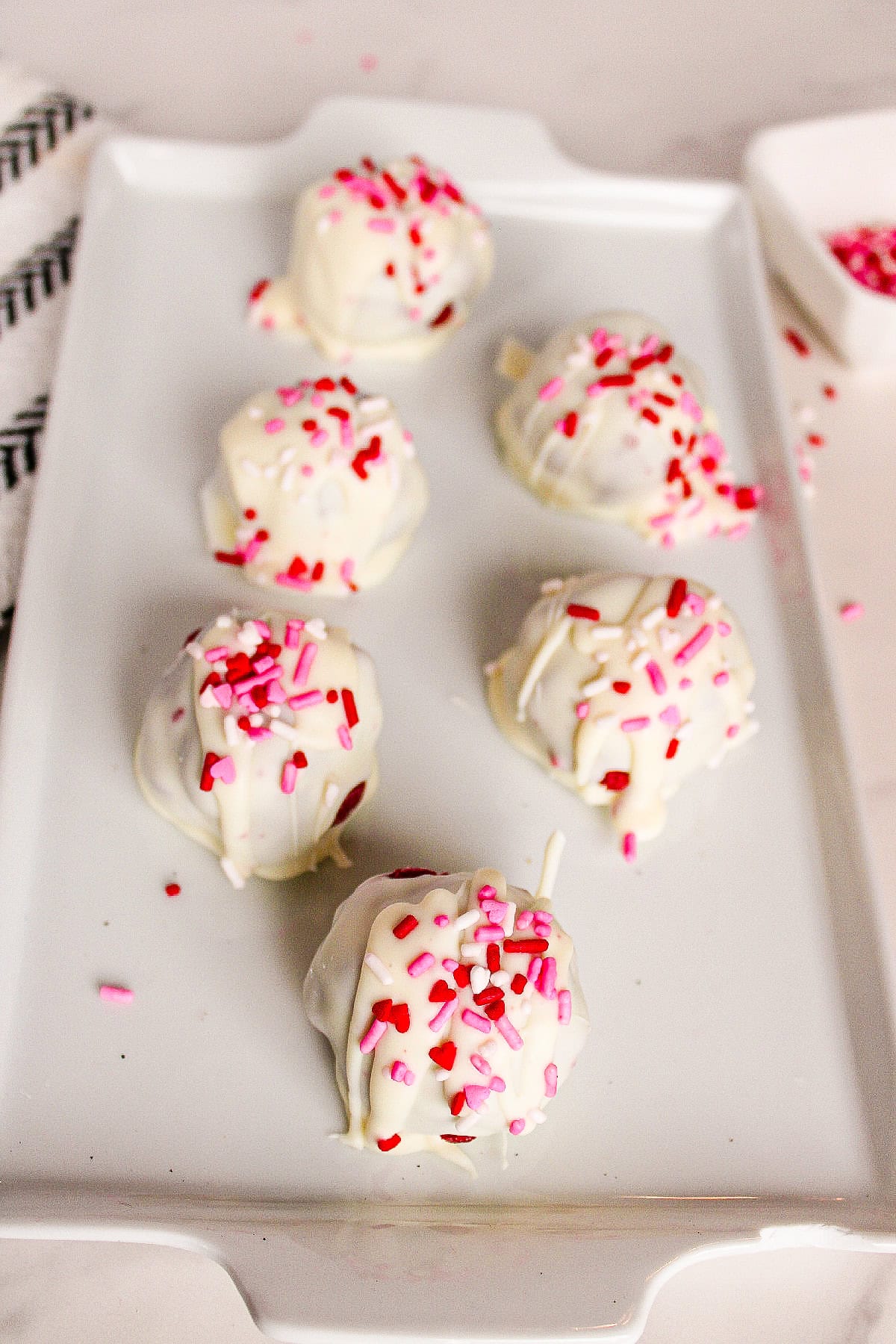 White chocolate red velvet truffles arranged on a white rectangular serving plate with pink and red sprinkles.