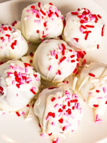 White chocolate red velvet truffles topped with pink and red sprinkles on a white plate.
