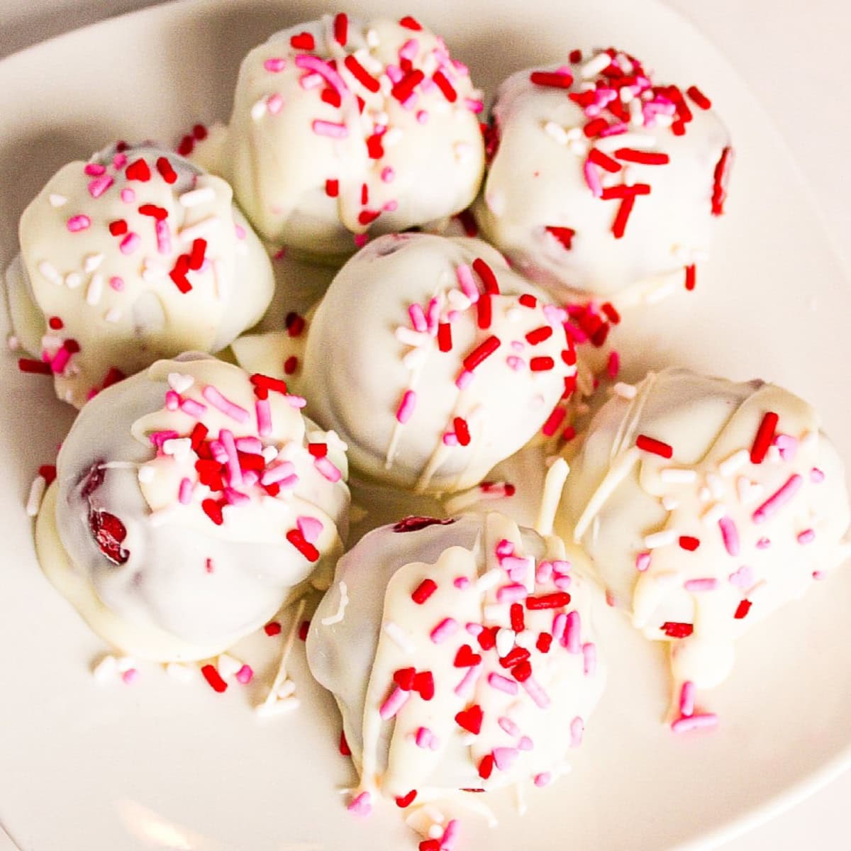 White chocolate red velvet truffles topped with pink and red sprinkles on a white plate.