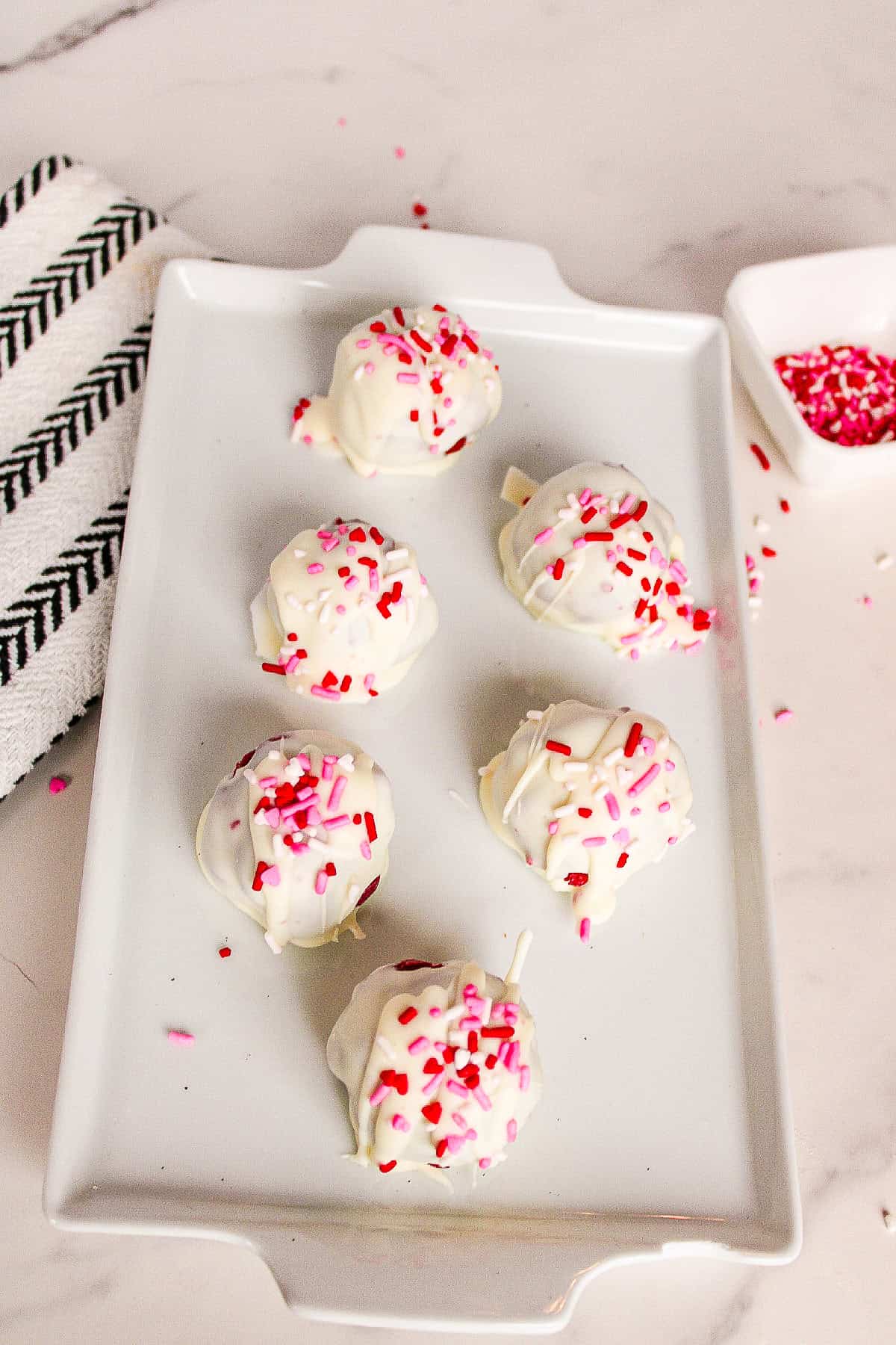 White chocolate red velvet truffles arranged on a white serving plate with festive sprinkles.