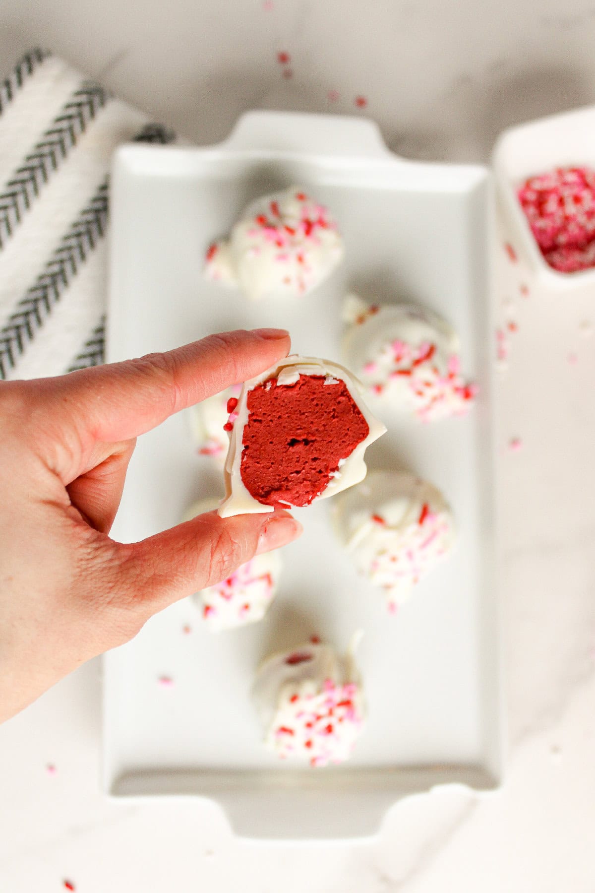 Hand holding a bitten red velvet truffle showing the soft red velvet center inside.