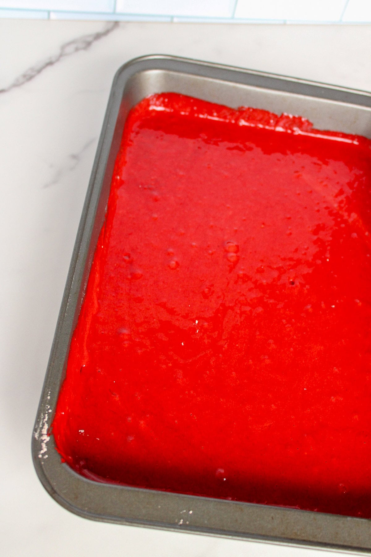 Unbaked red velvet cake batter spread evenly in a rectangular baking pan.