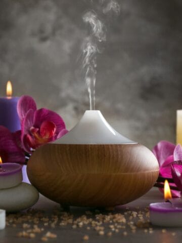 An essential oil diffuser gently emits mist amid glowing candles, orchids, and smooth spa stones for a soothing atmosphere.