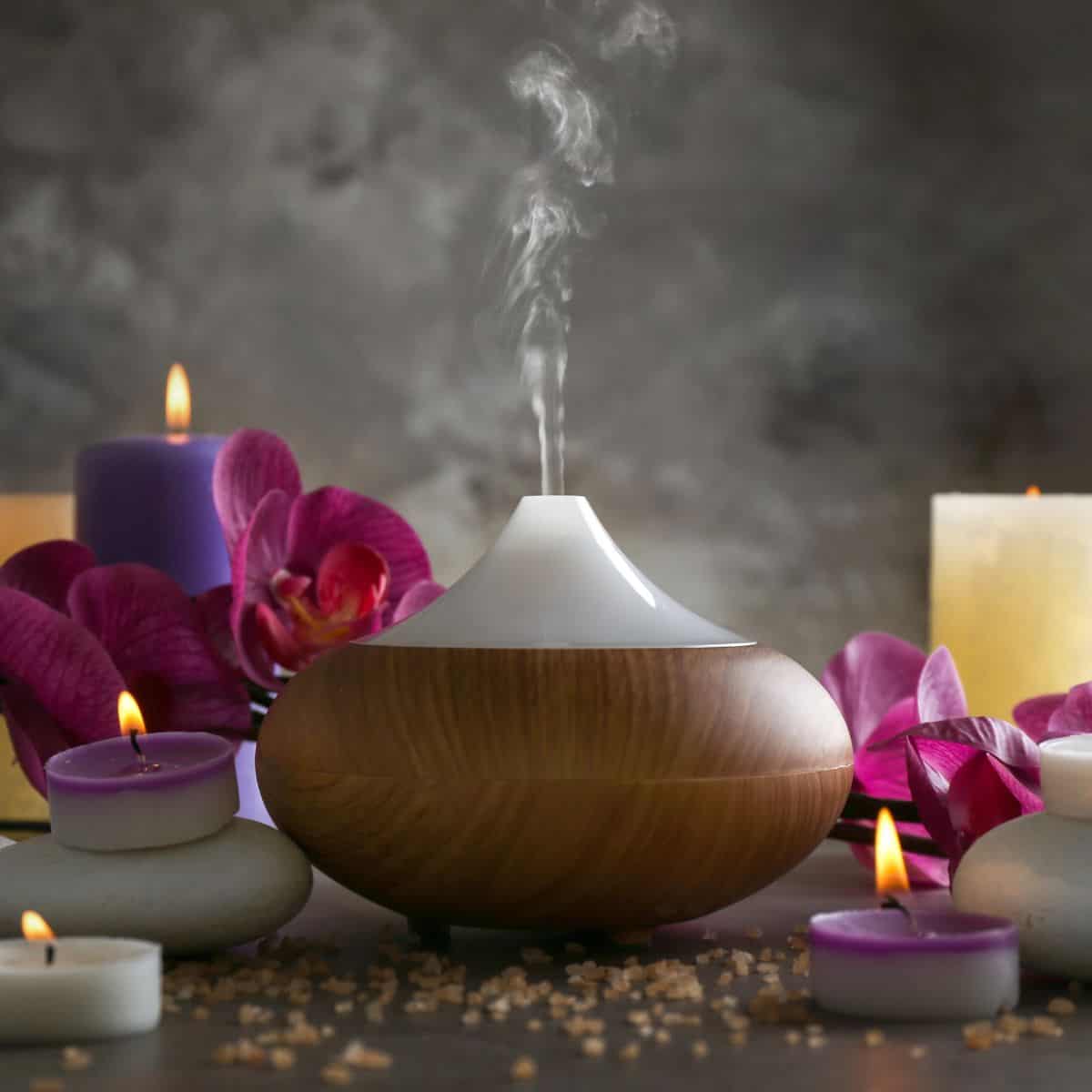 An essential oil diffuser gently emits mist amid glowing candles, orchids, and smooth spa stones for a soothing atmosphere.