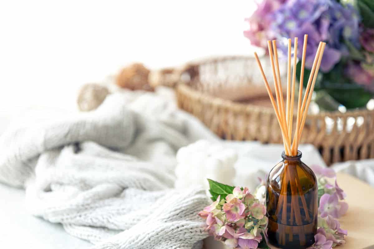 A reed diffuser in a glass bottle with wooden sticks and flowers on a soft, cozy surface.