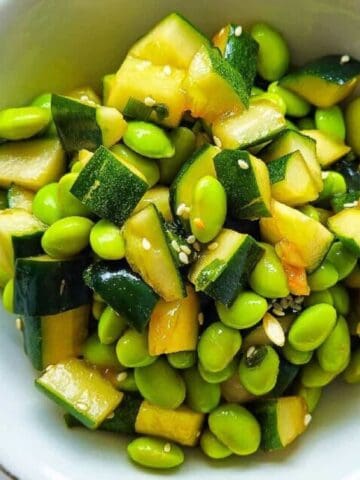 Close-up top view of cucumber and edamame salad in white bowl.