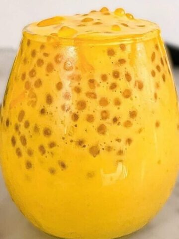 A glass of mango sago dessert topped with tapioca pearls, set on a marble countertop.