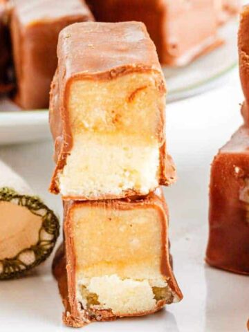 Chocolate coated Twix protein bars with two broken in half and stacked on top of each other.