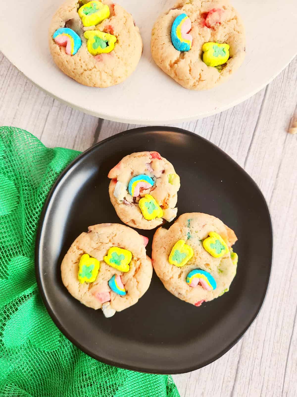 Homemade Lucky Charms cookies on a black plate with green cloth and cereal pieces.
