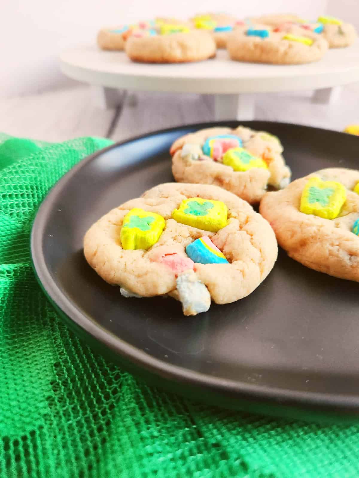 Lucky Charms cookies on a white serving stand with bright cereal marshmallows.