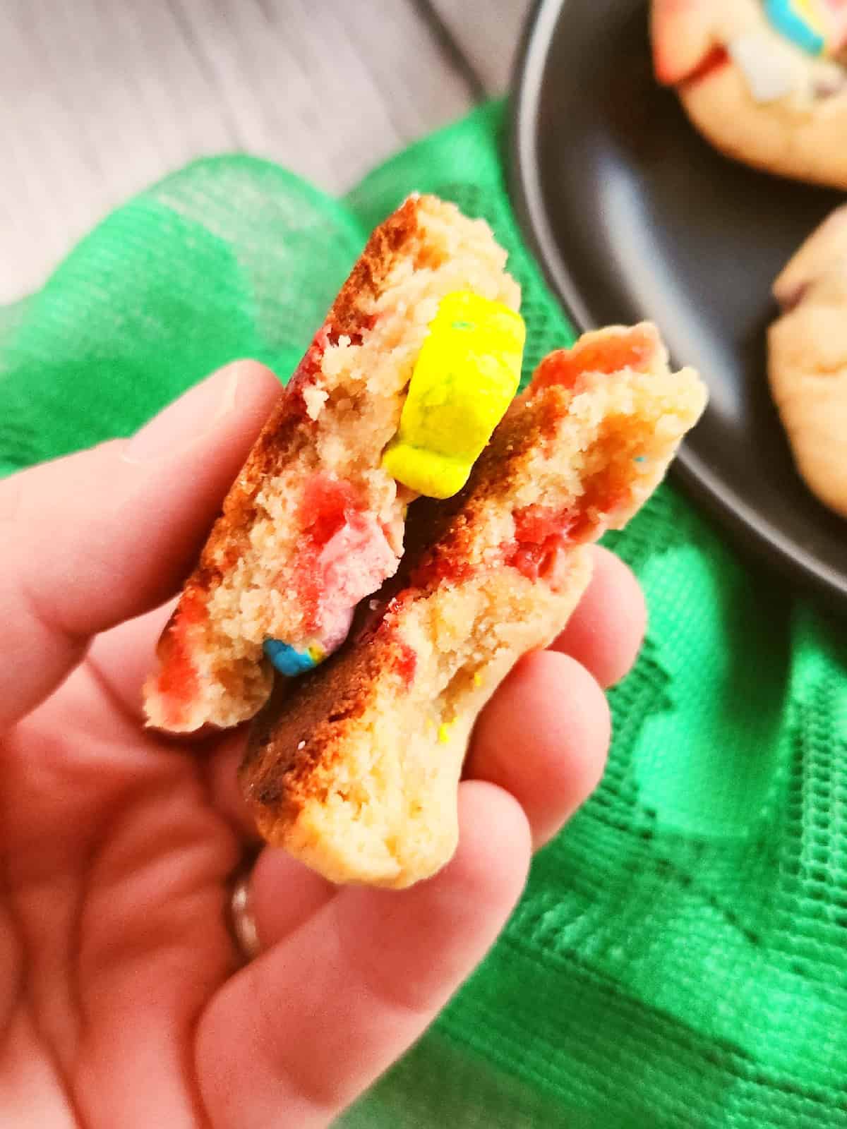 Hand holding a soft Lucky Charms cookie with rainbow cereal marshmallows.