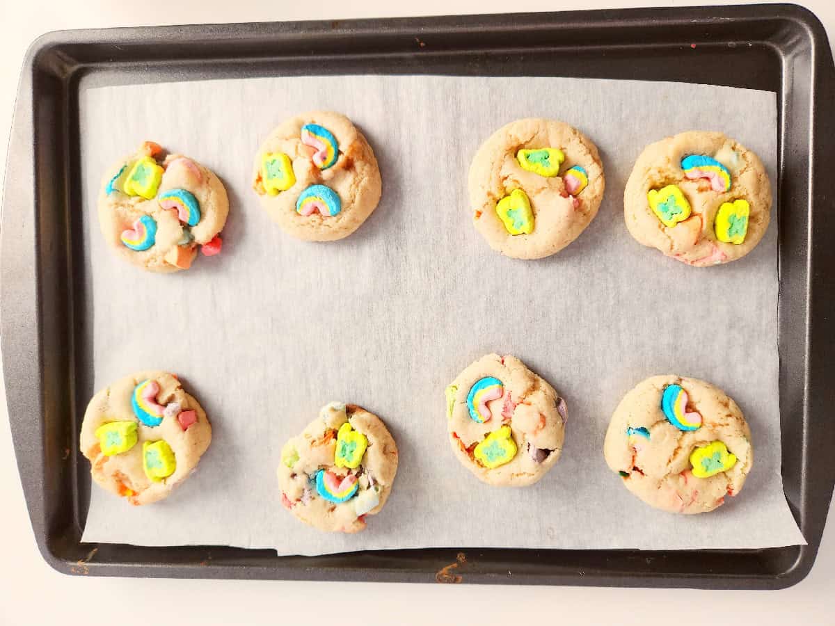 Lucky Charms cookies baked on a parchment-lined baking sheet with colorful marshmallow pieces on top.