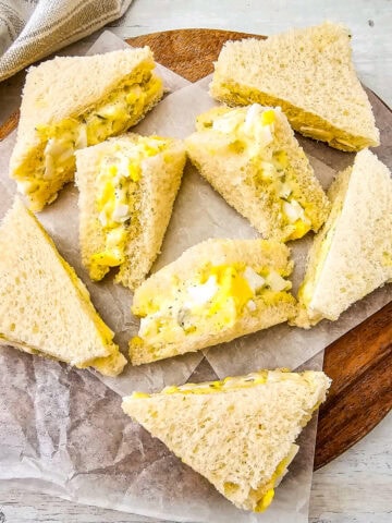 Close-up of egg salad tea sandwiches on white bread, cut into triangles with creamy egg and dill filling.