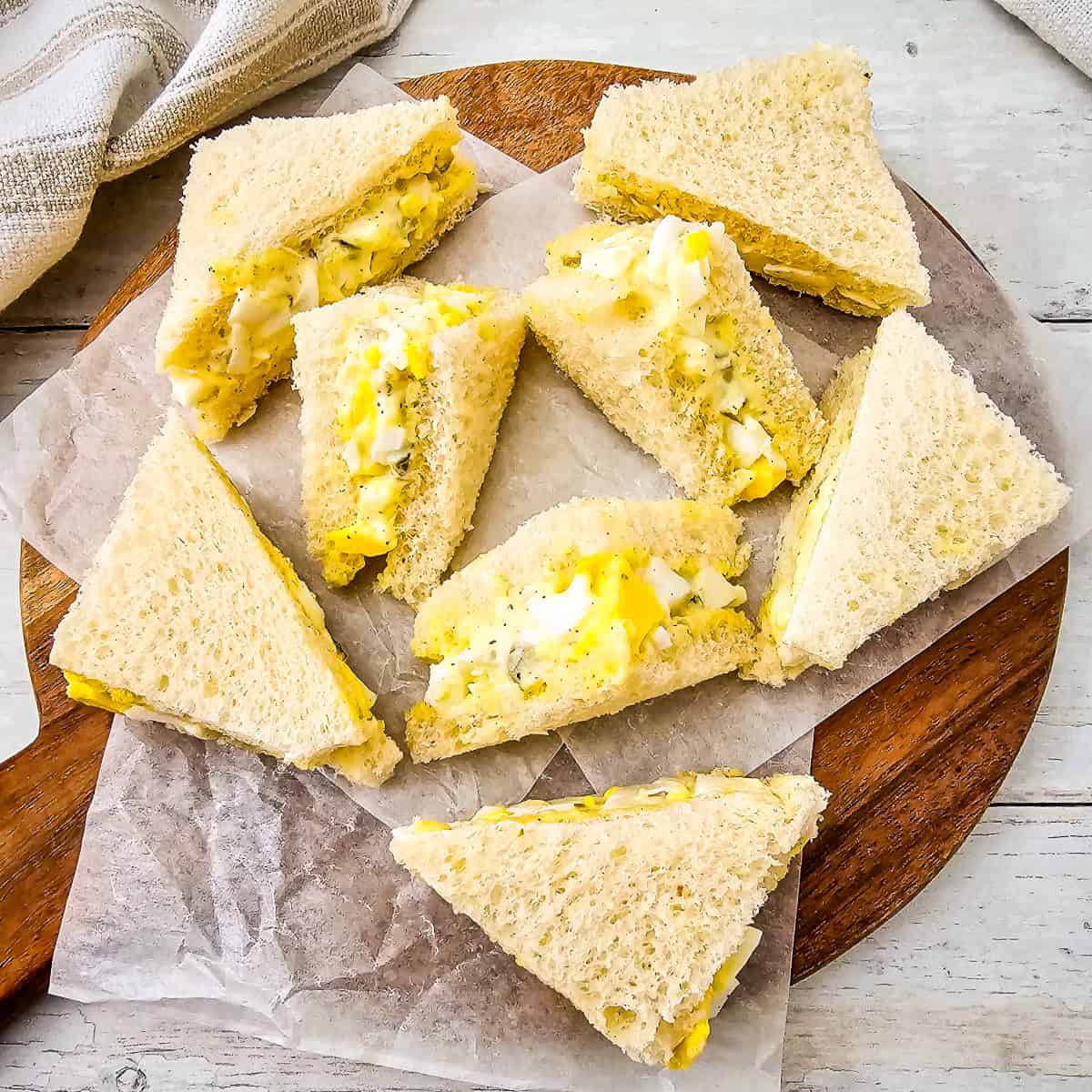 Close-up of egg salad tea sandwiches on white bread, cut into triangles with creamy egg and dill filling.