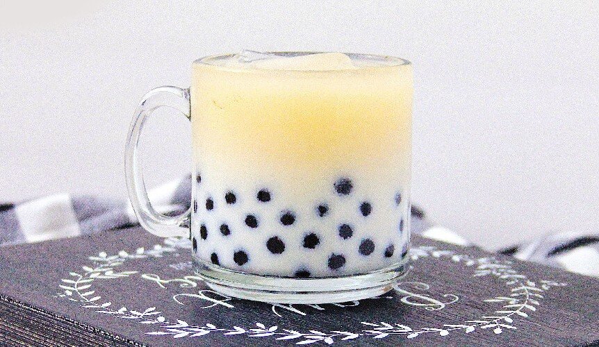 Iced milk tea with black tapioca pearls in a glass mug on wooden board.
