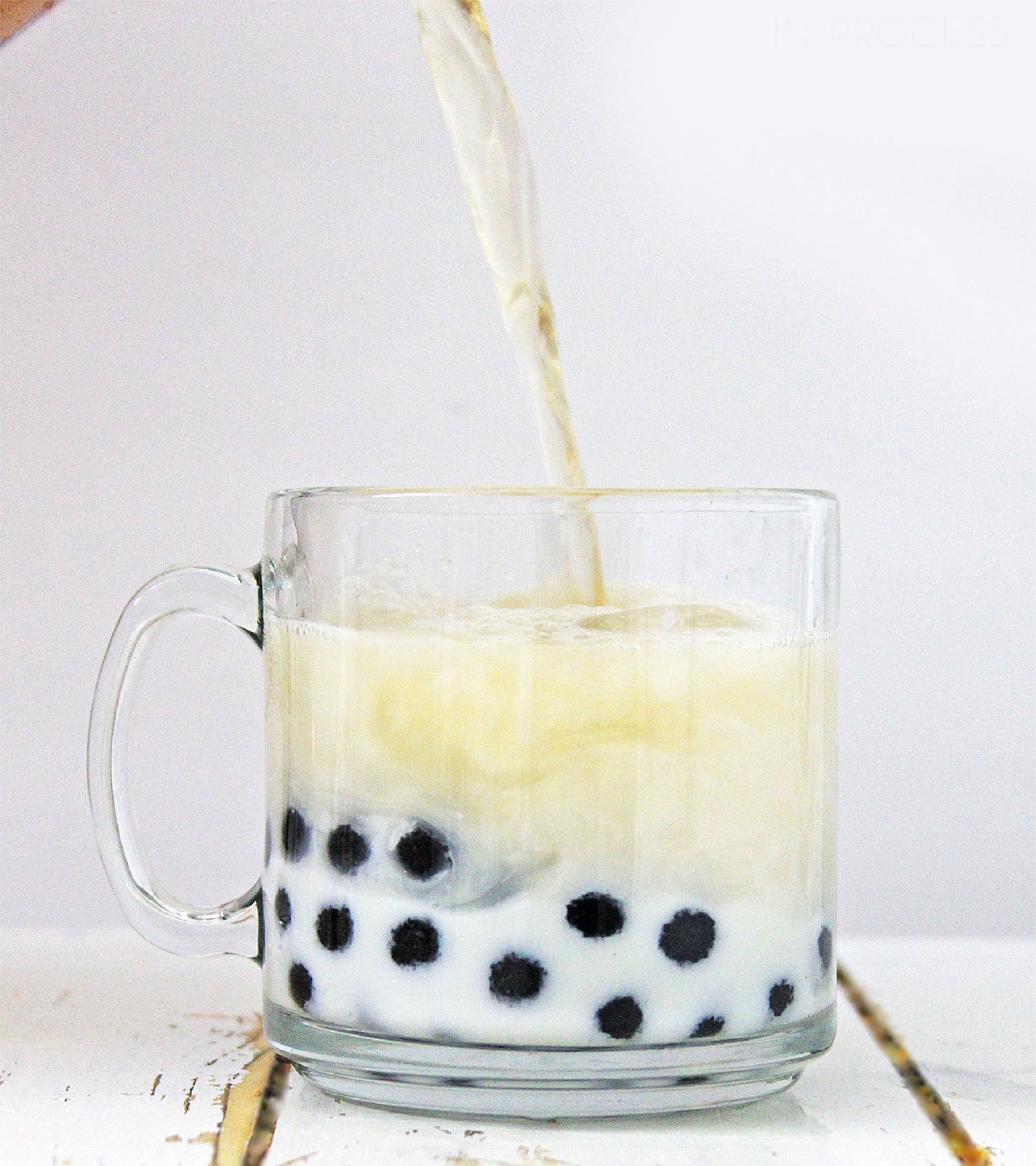 Freshly brewed tea being poured into milk and boba pearls.