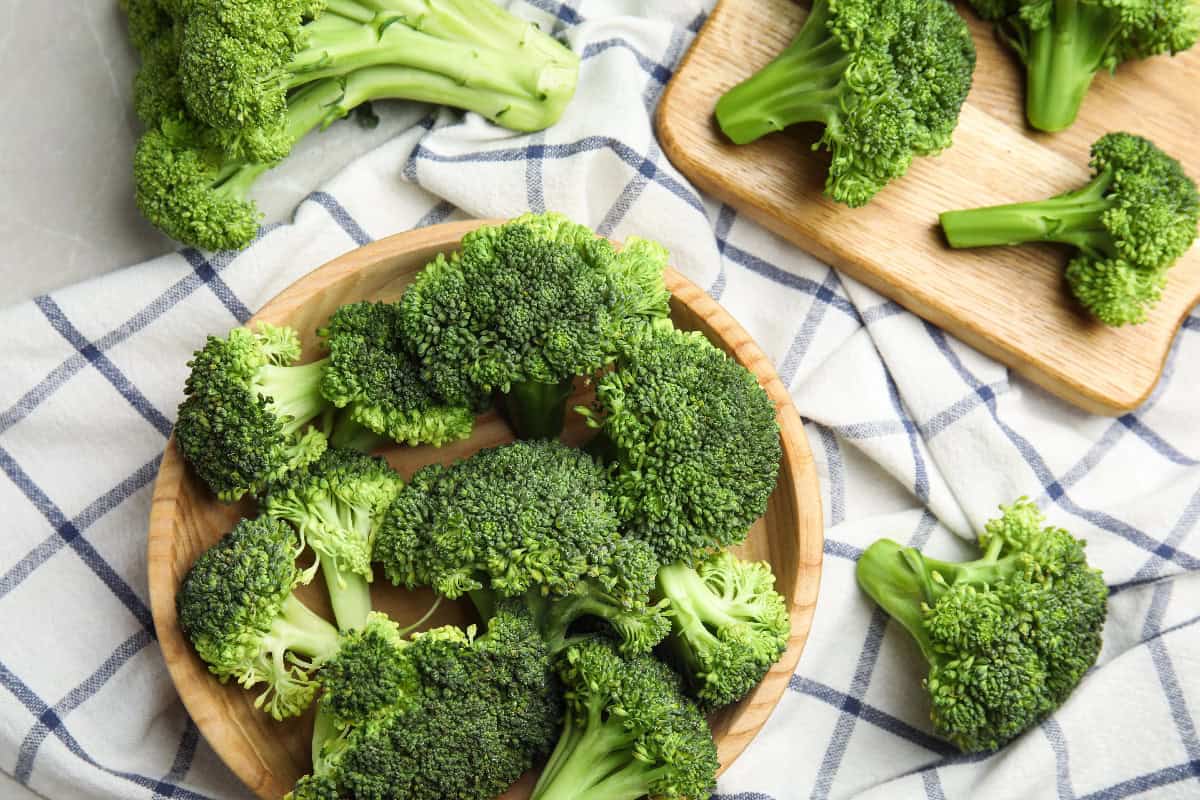 Broccoli florets in a wooden bowl on a kitchen cloth, a popular green vegetable.