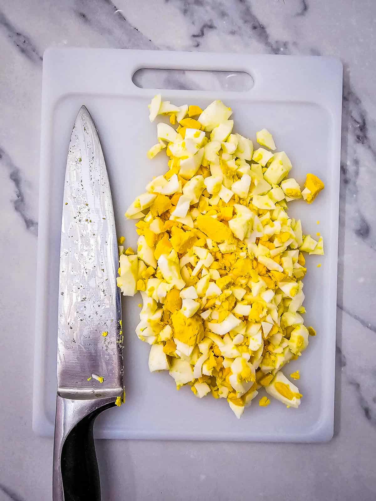 Finely chopped dill pickles on a white cutting board with a chef's knife.