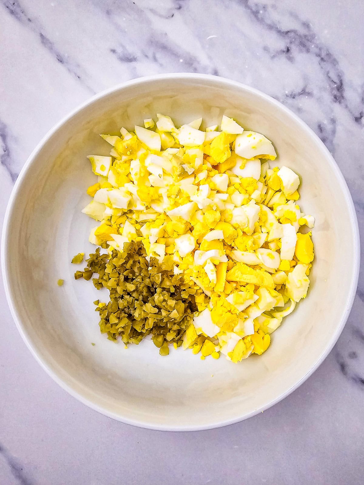 Chopped eggs and diced pickles in a bowl, ready to be mixed for egg salad.