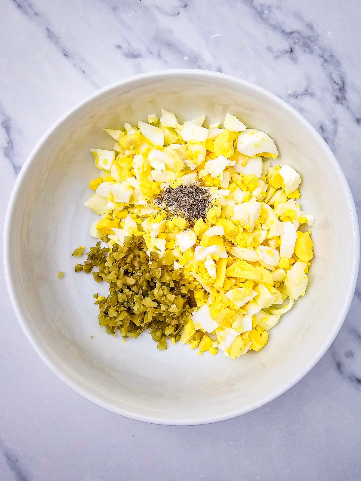 Chopped eggs and diced pickles in a bowl, ready to be mixed for egg salad.
