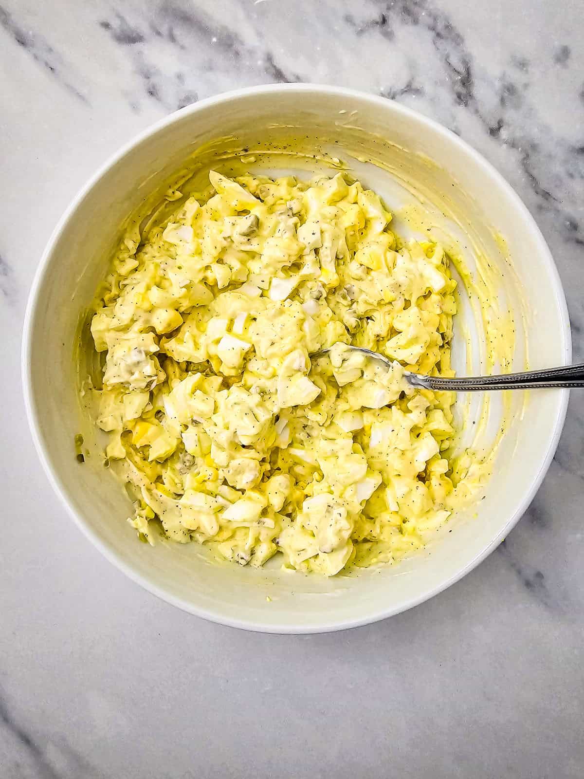 Creamy egg salad mixture fully combined in a bowl with a spoon.