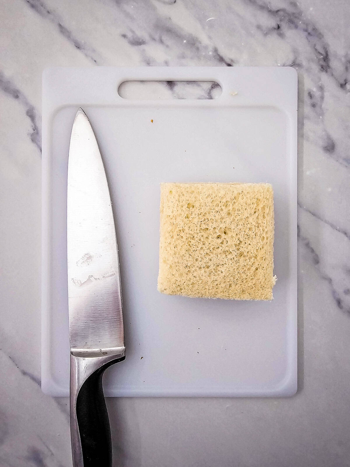 Crustless white bread cut into squares on a cutting board for tea sandwiches.