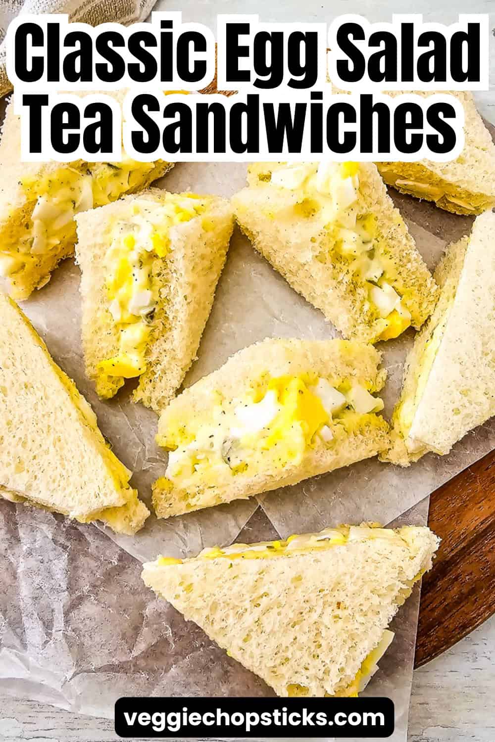 Egg salad tea sandwiches on a wooden board with soft bread and rich egg filling.