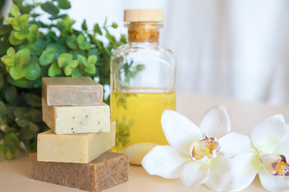 Natural vegan skincare products including handmade soap, plant oil, and flowers on a clean surface.