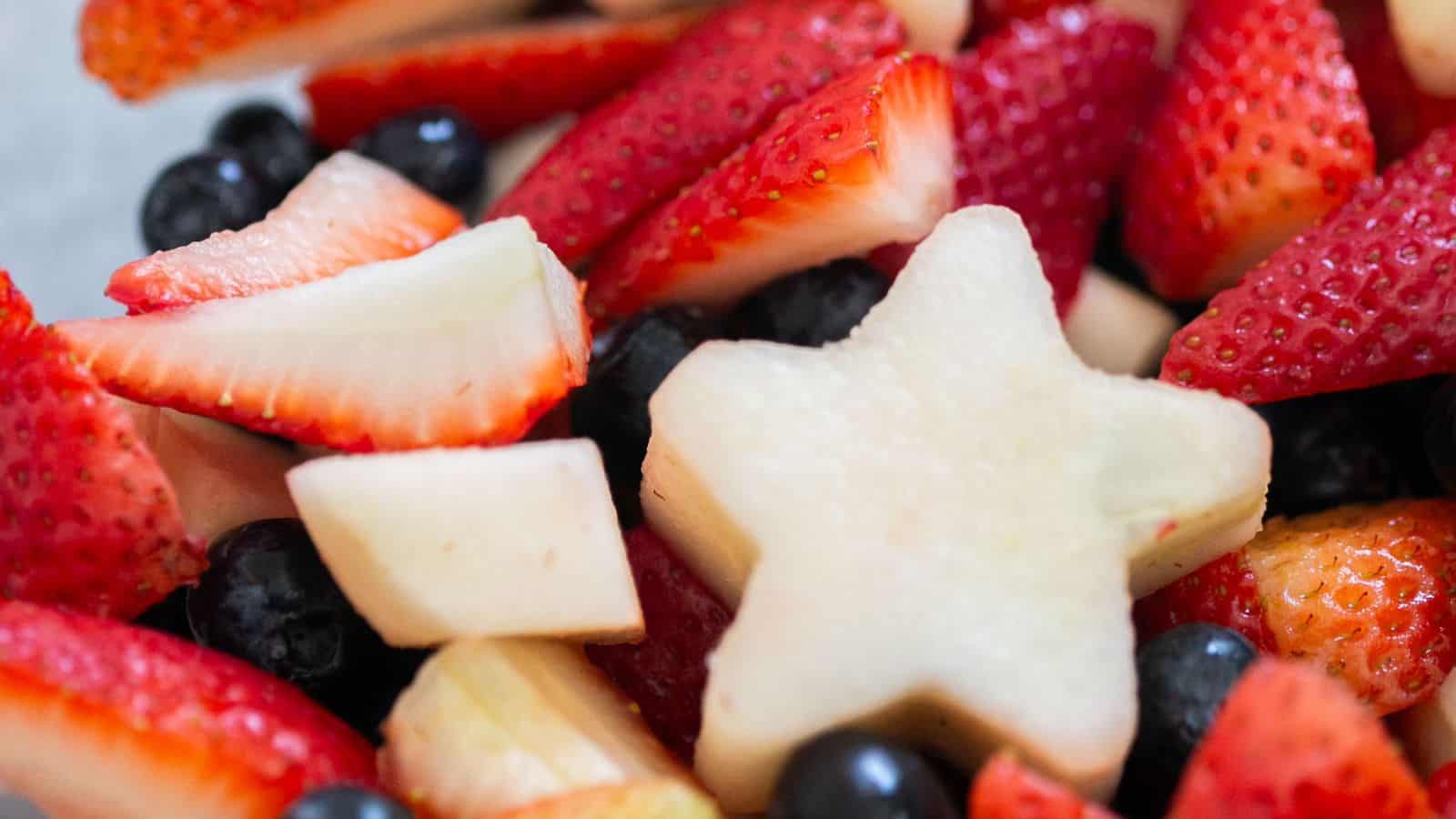 Fruit salad mixed with red, white, and blue berries in a festive bowl.