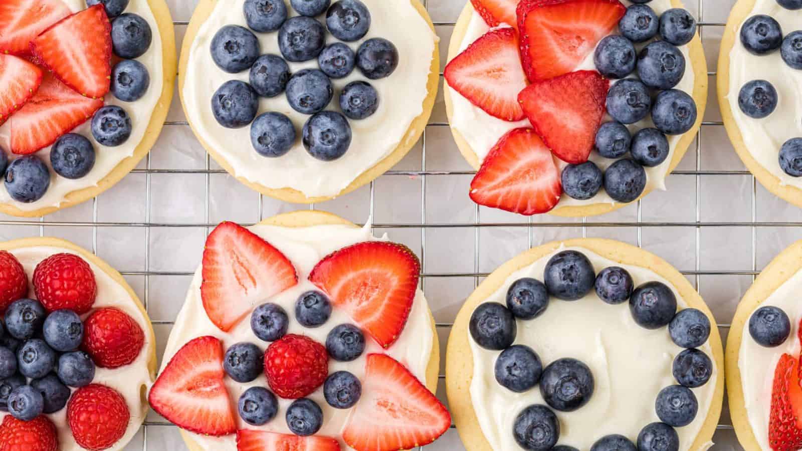 Fruit pizza cookies topped with berries and creamy frosting on soft cookie bases.