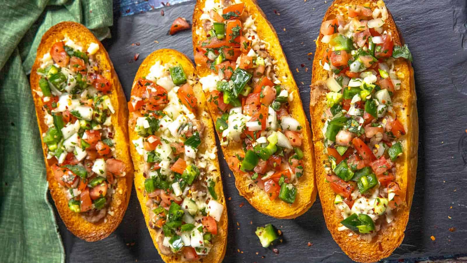 Molletes topped with beans, cheese, and fresh toppings on toasted bread.