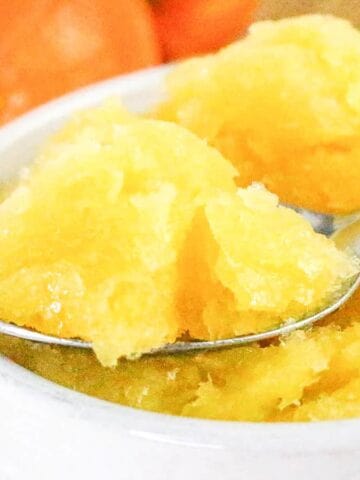 Fresh orange sorbet scooped into a white bowl with a spoon.
