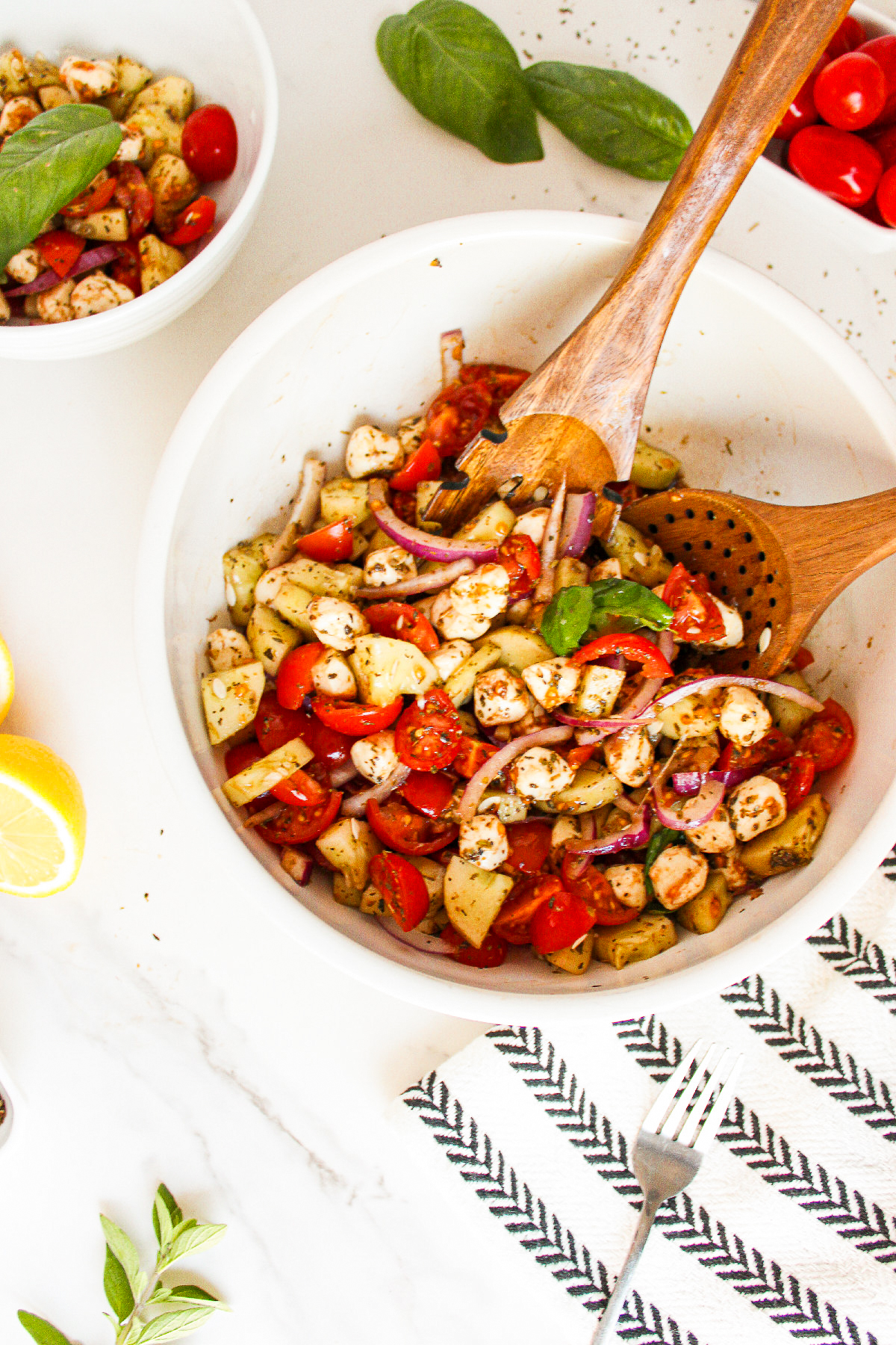 Alt Text: Overhead view of cucumber caprese salad tossed in a white bowl with cherry tomatoes, vegan mozzarella pearls, red onion, fresh basil, and rice vinegar herb dressing.