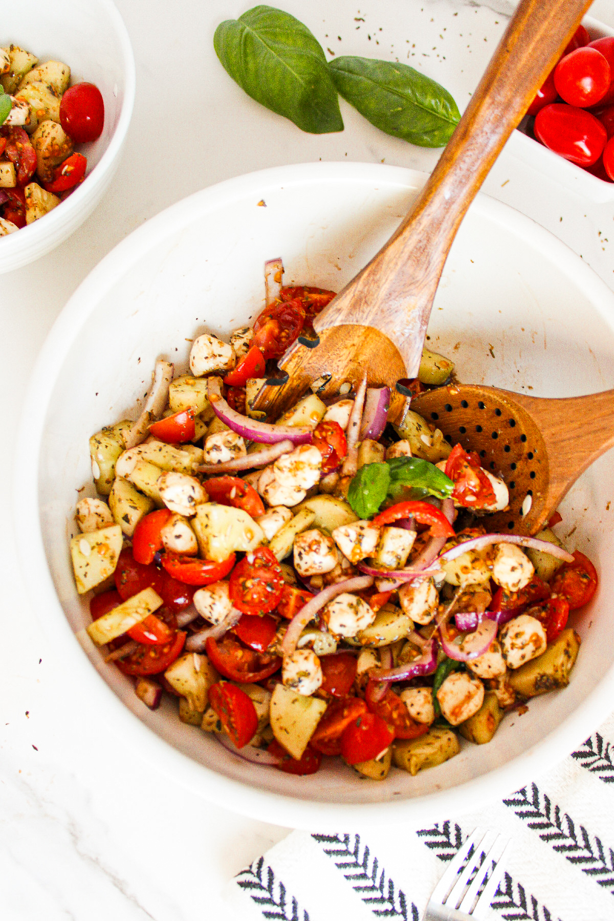 Ingredients for cucumber caprese salad arranged in white bowls, including chopped cucumber, cherry tomatoes, red onion, vegan mozzarella pearls, and dried herbs.