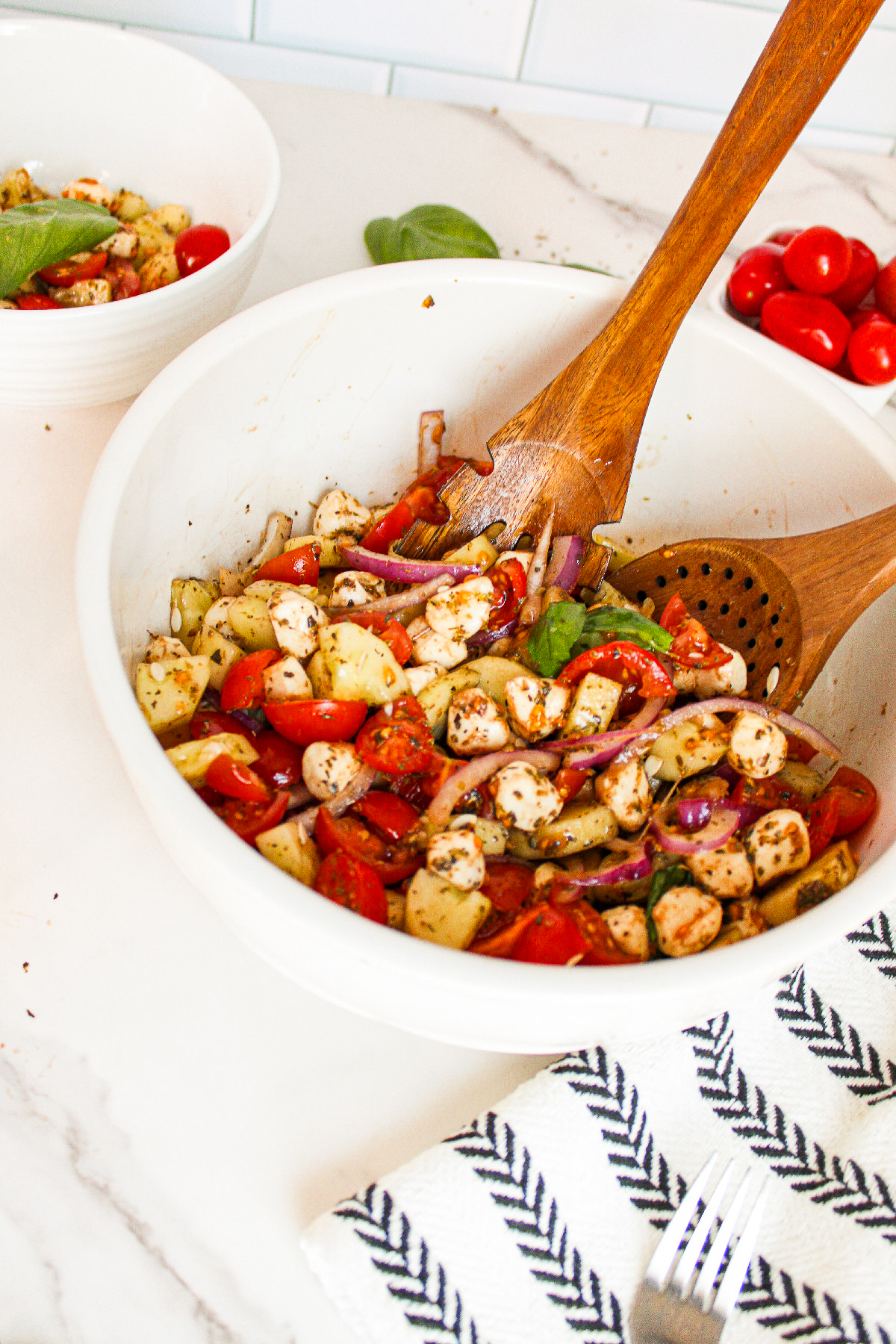 Cucumber caprese salad ingredients layered in a wooden bowl with chopped cucumber, cherry tomatoes, red onion, vegan mozzarella pearls, and fresh basil.